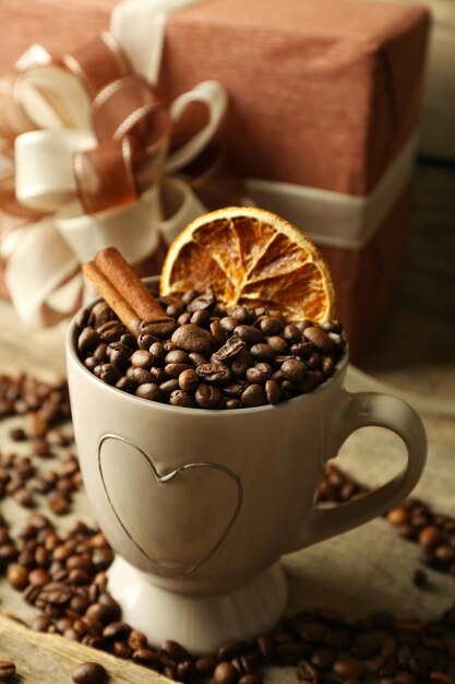 Beautiful gift with bow and coffee grains in mug, on wooden background