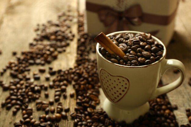 Beautiful gift with bow and coffee grains in mug, on wooden background