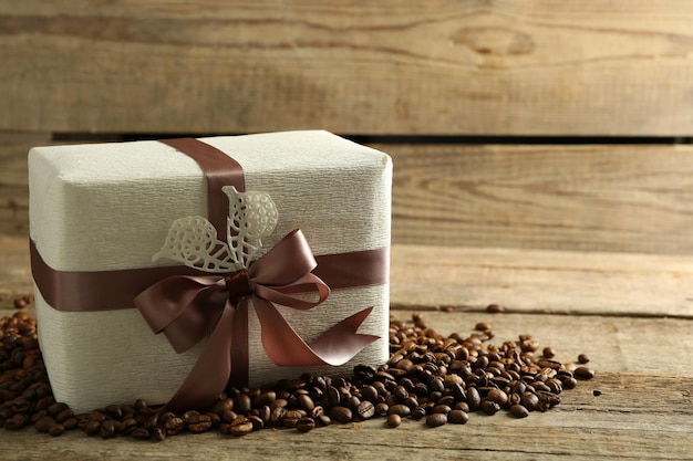 Красивый подарок с луком и кофейными зернами на деревянном фоне