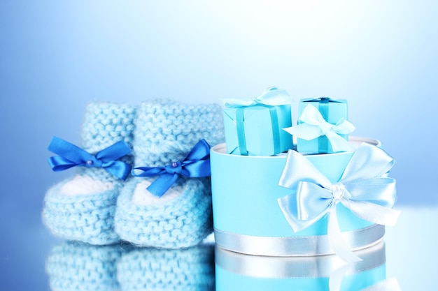 Photo beautiful gifts and baby's bootees on blue background