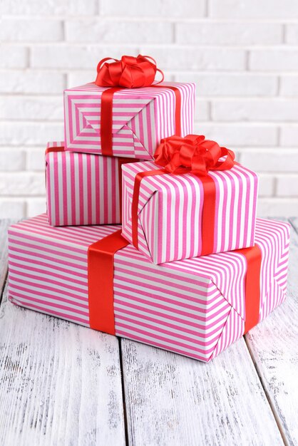 Photo beautiful gifts on table on brick wall background