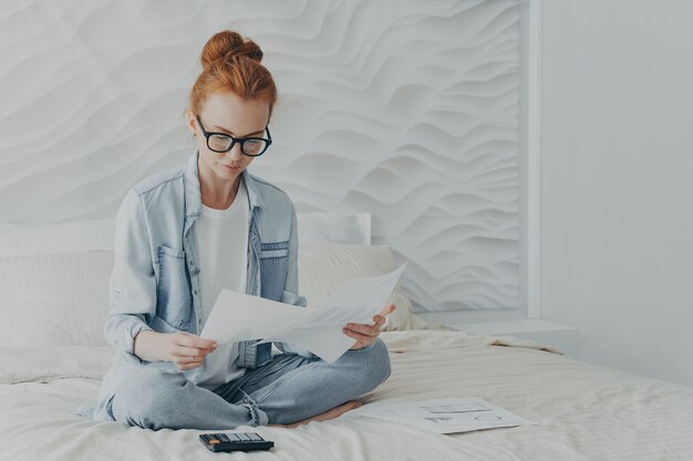 Photo beautiful ginger woman freelancer looks attentively at documents calculates manages finances