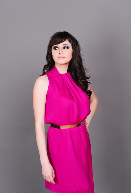 Beautiful girl 20-24 year old posing in studio over gray. Wearing pink dress. Spring season. 20s.