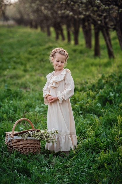 Beautiful girl 6-7 year old posing in garden in white dress. Easter time. enjoys spring and warmth. Happy childhood, peace and happiness concept. Aromatic blossom and retro vintage.