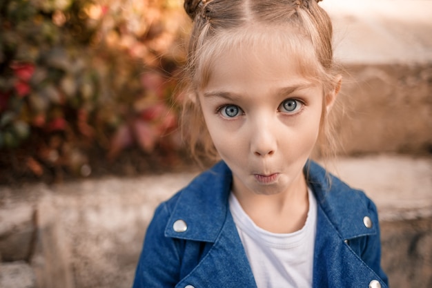 A beautiful girl of about seven in a denim jacket looks at the camera and makes faces