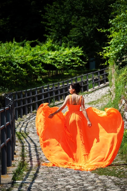 Beautiful girl in amazing fluttering orange dress standing on the cobblestone curved road