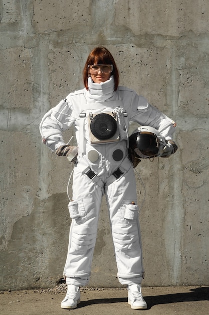 Beautiful girl astronaut without a helmet on the background of a gray wall. Fantastic space suit.