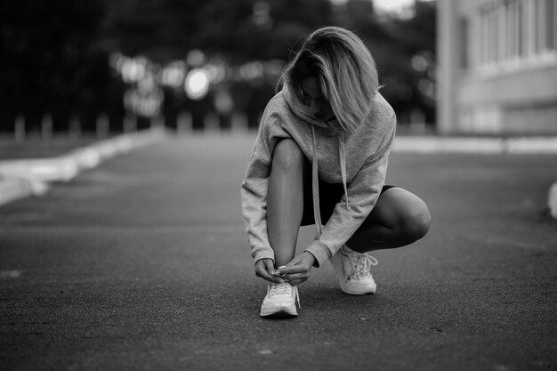 beautiful girl athlete sitting tying shoelaces on white sneakers black and white photo