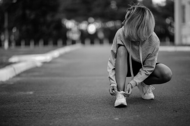 Beautiful girl athlete sitting tying shoelaces on white\
sneakers black and white photo