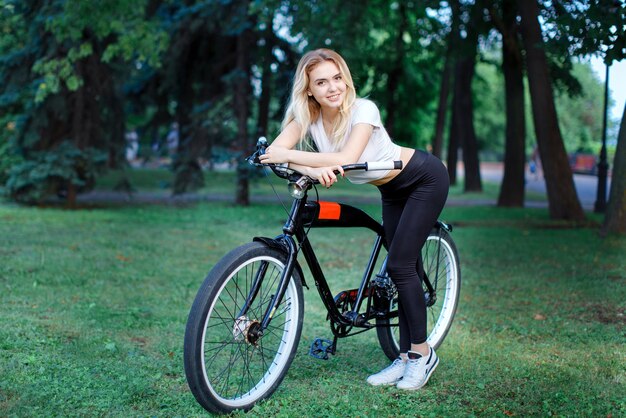 公園で自転車を持ったアスレチックビルドの美しい少女が笑顔でカメラに向かってポーズをとる