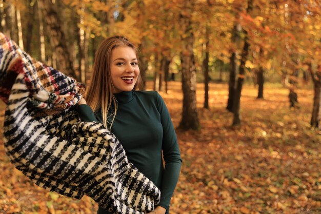 Красивая девушка в осеннем парке улыбается, держа в руках шарф
