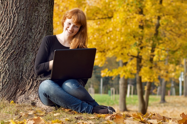 The beautiful girl in autumn park with the laptop