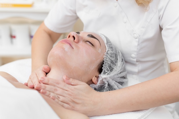 Bella ragazza dall'estetista fa le procedure termali, massaggio facciale e maschera per la pelle.