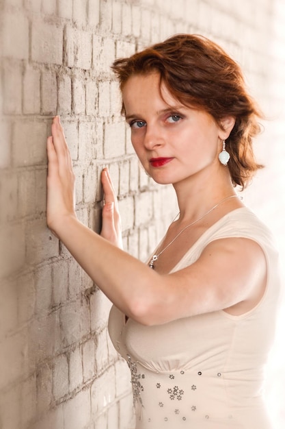 Bella ragazza in un vestito beige su uno sfondo di muro di mattoni