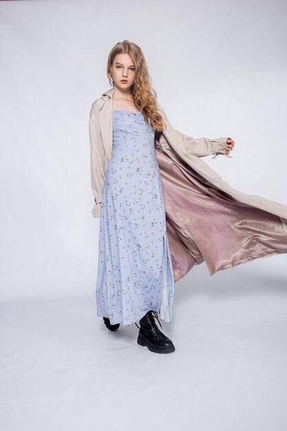 Beautiful girl in beige raincoat posing in Studio on grey background