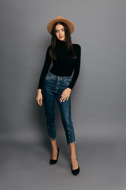 Beautiful girl in black body suit, jean and straw hat, isolated on grey background