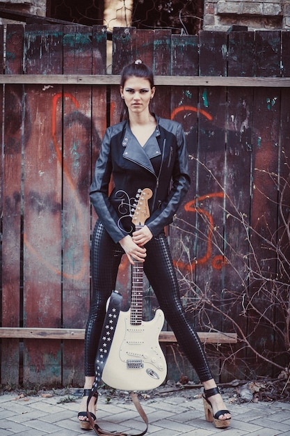 Beautiful girl in black clothes poses with electric guitar