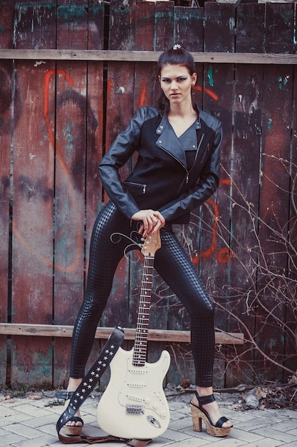 Beautiful girl in black clothes poses with electric guitar