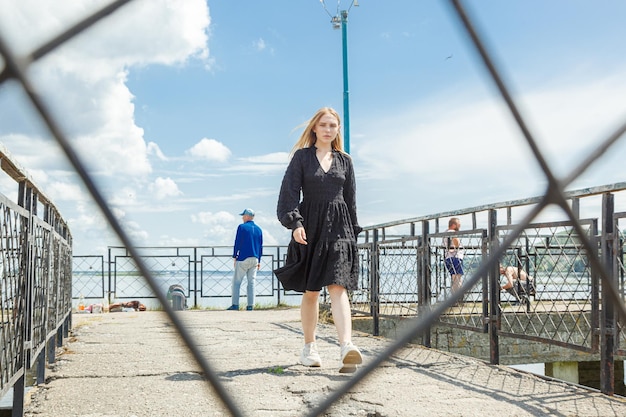 Beautiful girl in a black dress on the background of the river sea with blue sky and clouds