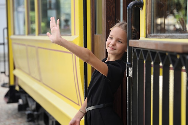 Beautiful girl in a black dress gets out of the tram and waves her hand
