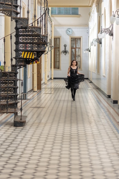 Красивая девушка в черном платье бежит по клетчатому полу в зале