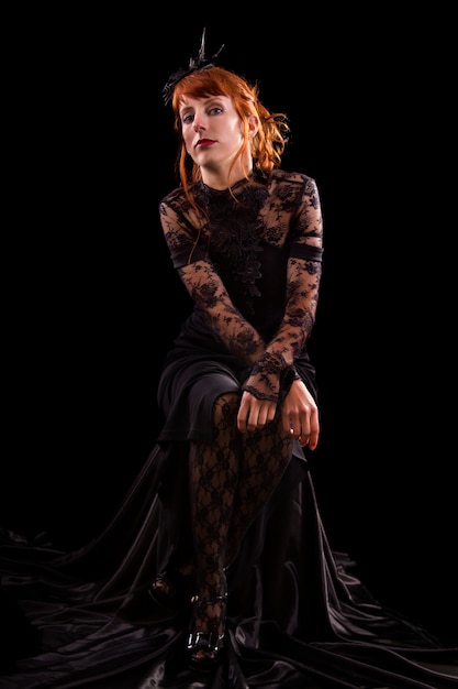 Beautiful girl on a black gothic dress with red hair isolated on a black background.