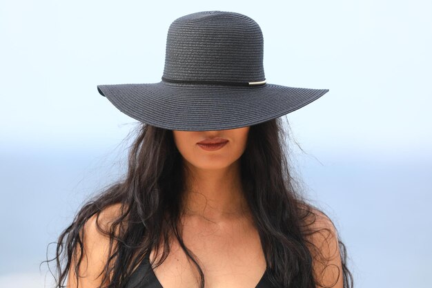 Foto bella ragazza con un cappello nero e bikini sulla spiaggia