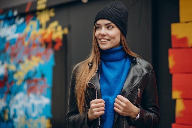 Beautiful girl in black jacket standing by colorful wall