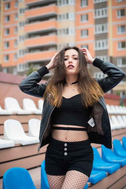 Beautiful girl in black shorts and a black leather jacket on the background of sports stands