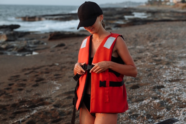 Красивая девушка в черном купальнике носит спасательный жилет на пляже