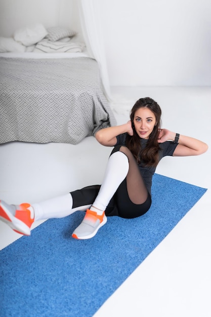 Beautiful girl in a black tracksuit is engaged in fitness at home Fitness girl doing exercises on the press A fit girl leading an active lifestyle Smiling looking at the camera