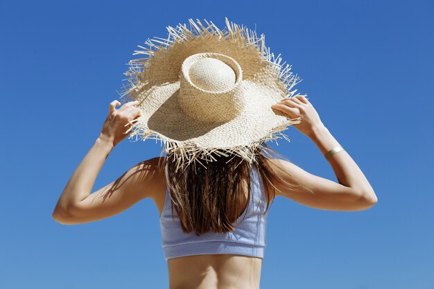 Beautiful girl in a blue bathing suit and straw hat on a background of blue sky