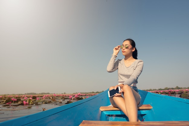 Beautiful girl on blue boat in pink lotus lake in the morning. Sun protection.