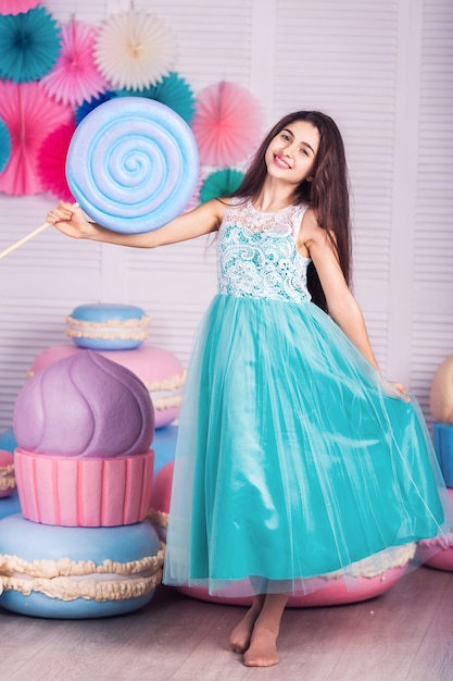 Beautiful girl in blue dress hold in hand huge candy with decor of macaroons