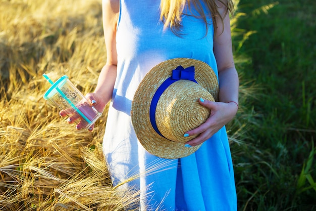 Красивая девушка в голубом платье держит в руках стакан и шляпу