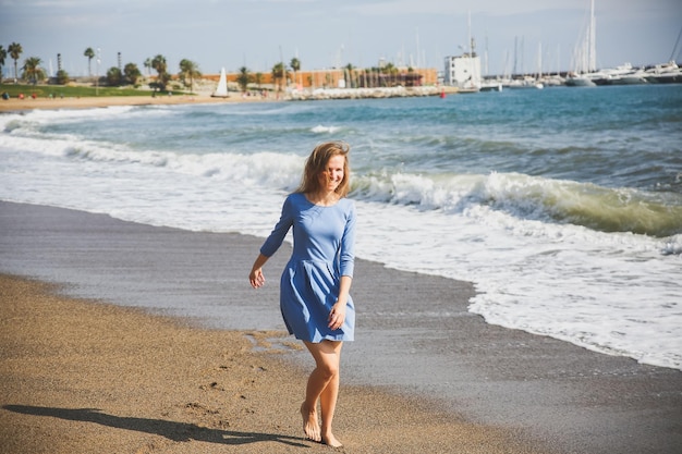 青いドレスを着た美しい女の子がビーチを歩いています 素晴らしい夏の写真 海の近くで踊ったりジャンプしたりする女性 幸せで楽しい感情 休日の旅行のコンセプト スリムな脚 暖かい海の水