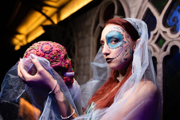 Bella ragazza in un vestito blu con trucco artistico sul viso tiene un teschio in mano maschera di halloween masquerade discoteca di halloween concept