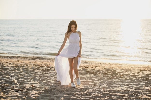 Bella ragazza sposa in abito bianco e scarpe da ginnastica, al tramonto passeggiate lungo la spiaggia.