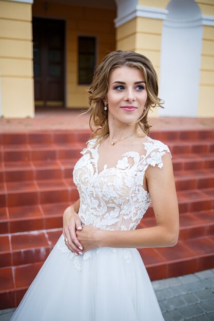 Beautiful girl bride in a white dress with a train walking on the background of a large house with columns on their wedding day