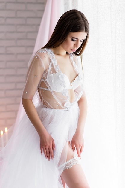 Bella ragazza sposa in un boudoir di pizzo bianco vestito di lino chiuso con un velo la mattina del giorno del matrimonio sullo splendido scenario dei fiori.