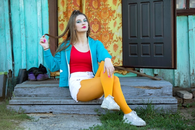 Photo a beautiful girl in bright clothes sits on the porch of a village house