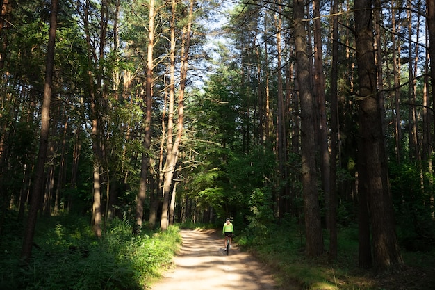 A beautiful girl in a bright green windbreaker, shorts and a helmet rides a bicycle in the forest