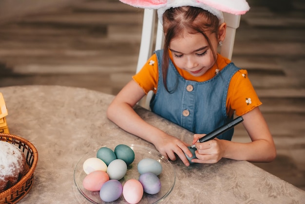 Bella ragazza in orecchie da coniglio dipingere le uova di pasqua