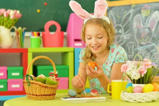 Beautiful girl in bunny ears painting eggs for Easter holiday