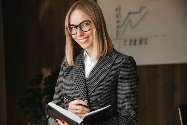 Beautiful girl businesswoman smiling happily while holding a notebook and a pen portrait of an office worker