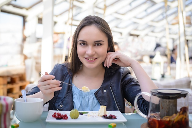 テーブルに座ってチーズケーキを食べるカフェの美しい女の子