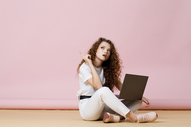 Beautiful girl in casual clothes and glasses sits on the floor and using laptop