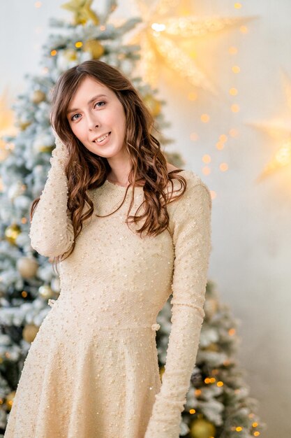 크리스마스 트리에서 아름다운 소녀 긴 머리를 가진 소녀 스타일링과 메이크업을 한 소녀 소녀를 위한 크리스마스 이브닝 드레스