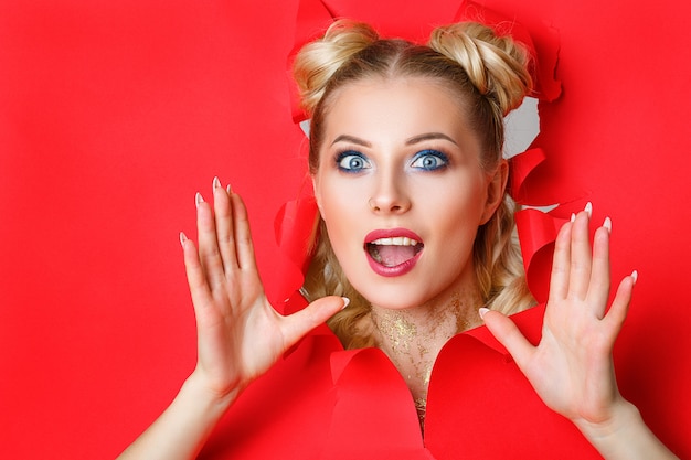 A beautiful girl in climbs out of a hole in red paper