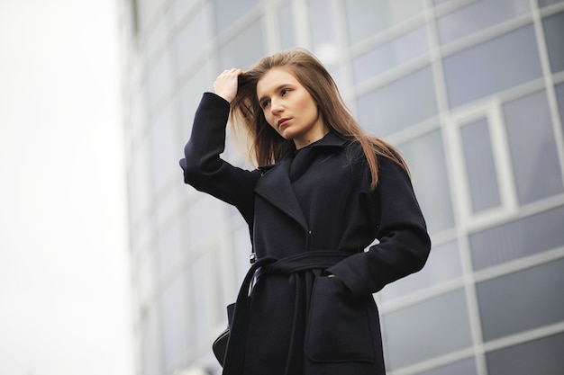 Photo beautiful girl in a coat in business downtown of the cloudy